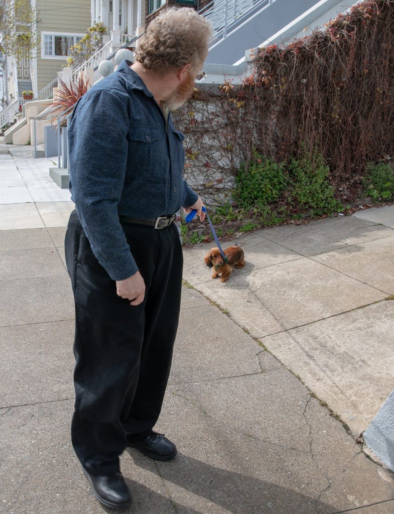 Auroara on a leash being held by Geoffrey. She's laying down in the driveway looking stubborn