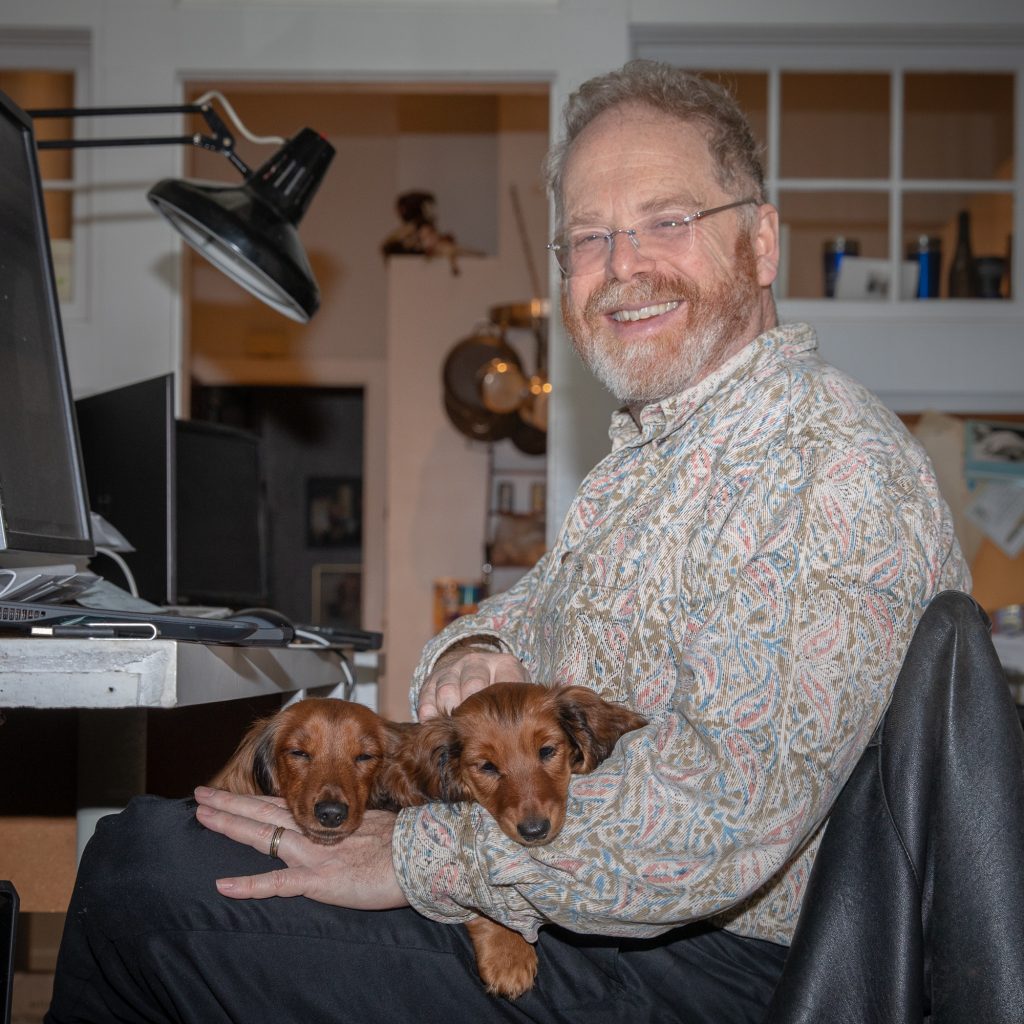 Geoffrey sitting at the computer with Zenith and Aurora on his lap